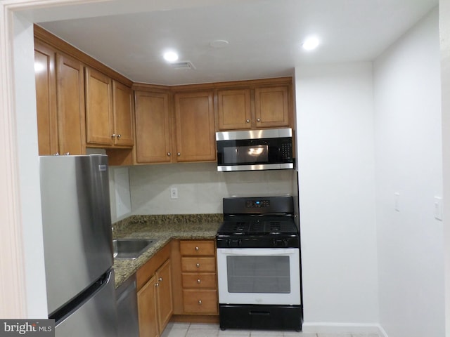 kitchen featuring stainless steel appliances, visible vents, brown cabinetry, a sink, and dark stone countertops