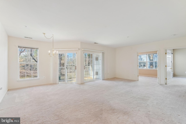 spare room featuring visible vents, light colored carpet, and an inviting chandelier