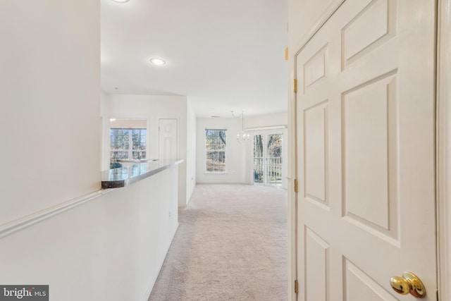 hall featuring light colored carpet and an inviting chandelier