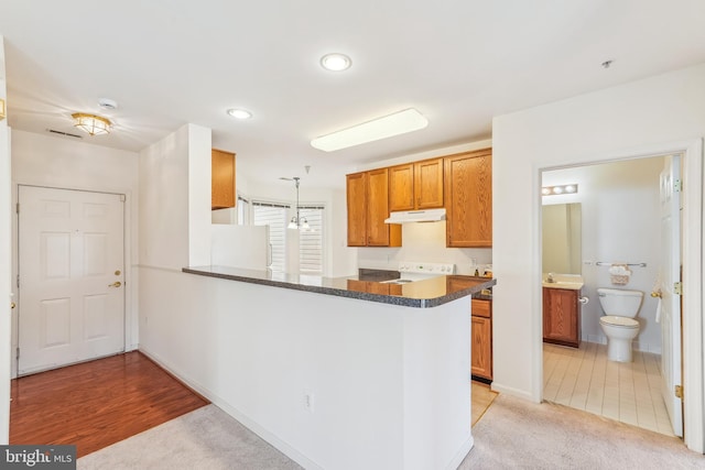 kitchen featuring pendant lighting, under cabinet range hood, dark countertops, a peninsula, and stove