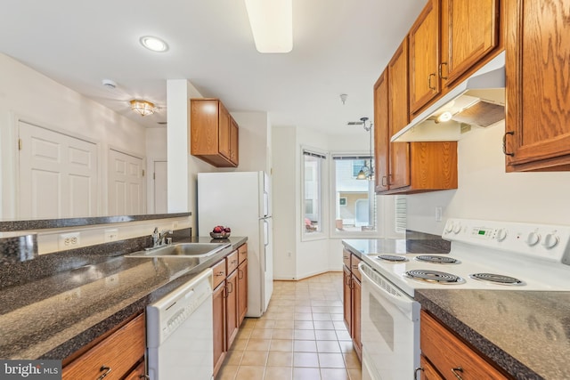 kitchen featuring under cabinet range hood, light tile patterned floors, brown cabinetry, white appliances, and a sink