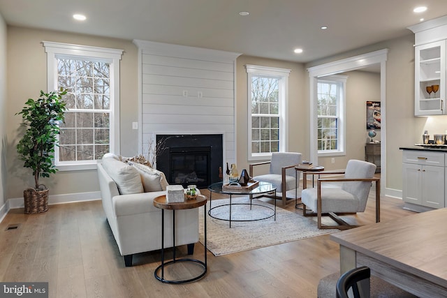 living room with light wood-type flooring, a glass covered fireplace, baseboards, and recessed lighting