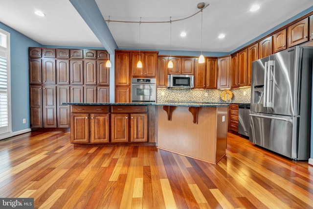 kitchen with appliances with stainless steel finishes, light wood-type flooring, a center island, tasteful backsplash, and a kitchen bar