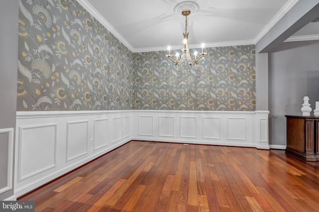 unfurnished dining area featuring wallpapered walls, ornamental molding, hardwood / wood-style floors, and wainscoting