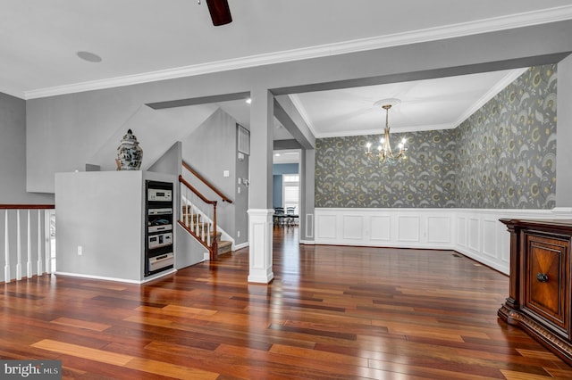 empty room with wallpapered walls, ornamental molding, wainscoting, a chandelier, and hardwood / wood-style flooring