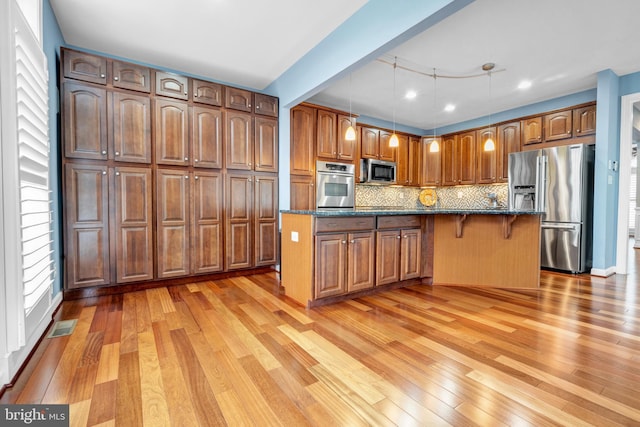 kitchen featuring light wood-type flooring, tasteful backsplash, dark stone counters, and stainless steel appliances