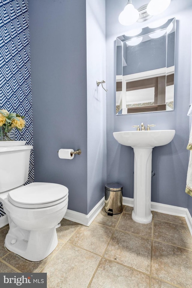 half bath with toilet, baseboards, and tile patterned floors