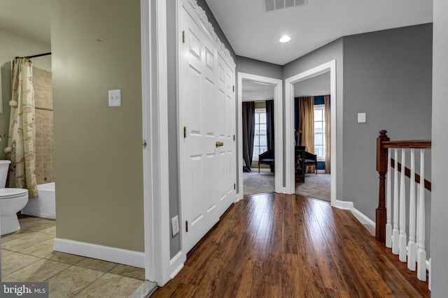 hallway featuring visible vents, baseboards, wood finished floors, and an upstairs landing