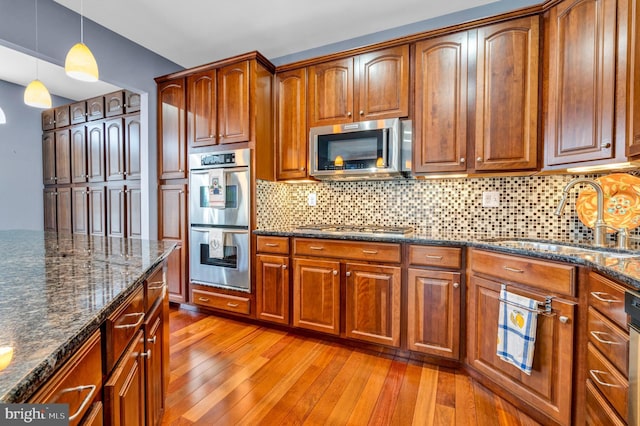 kitchen featuring decorative backsplash, decorative light fixtures, stainless steel appliances, light wood-style floors, and a sink