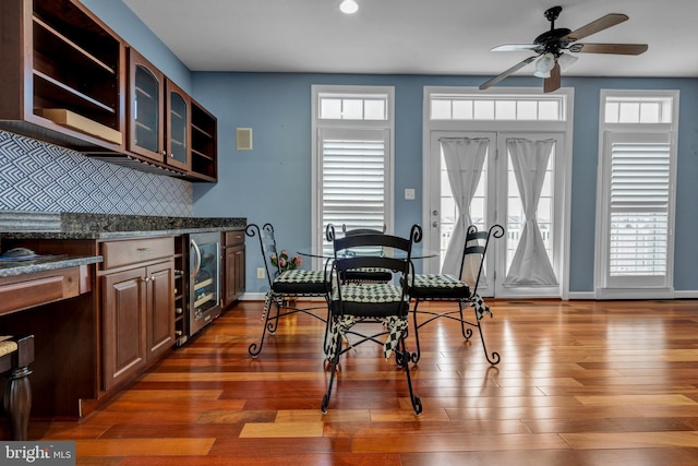 dining area with a ceiling fan, wine cooler, baseboards, and wood finished floors