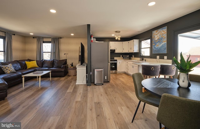 kitchen with open floor plan, stainless steel appliances, light countertops, white cabinetry, and a sink