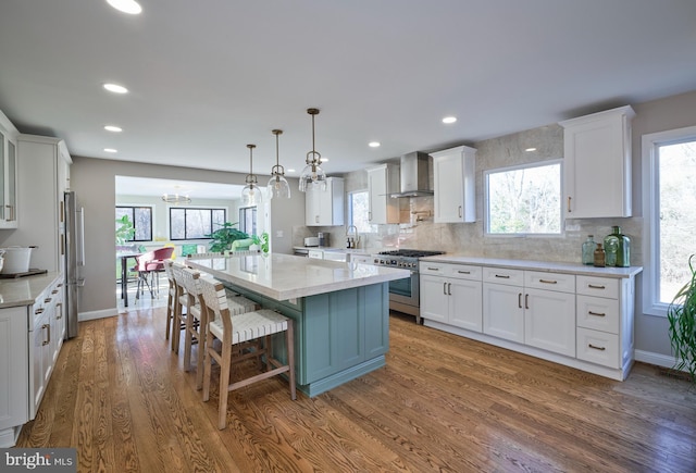 kitchen featuring white cabinets, wall chimney exhaust hood, a kitchen island, dark wood-type flooring, and stainless steel appliances