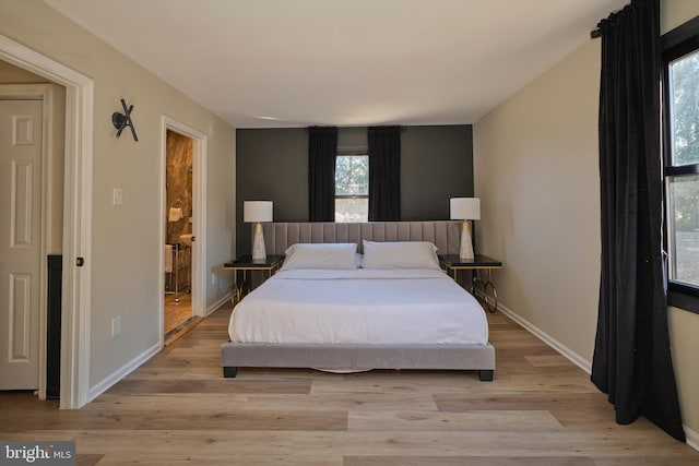 bedroom featuring ensuite bathroom, light wood-type flooring, and baseboards