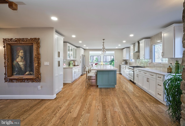 kitchen with wall chimney range hood, white cabinetry, stainless steel appliances, and light wood finished floors