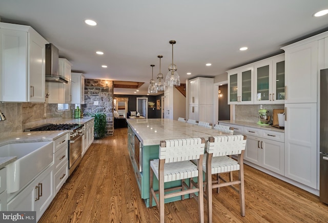 kitchen with stainless steel appliances, wall chimney range hood, a sink, and white cabinetry