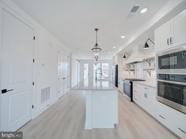 kitchen with visible vents, stainless steel range with gas stovetop, freestanding refrigerator, premium range hood, and a sink