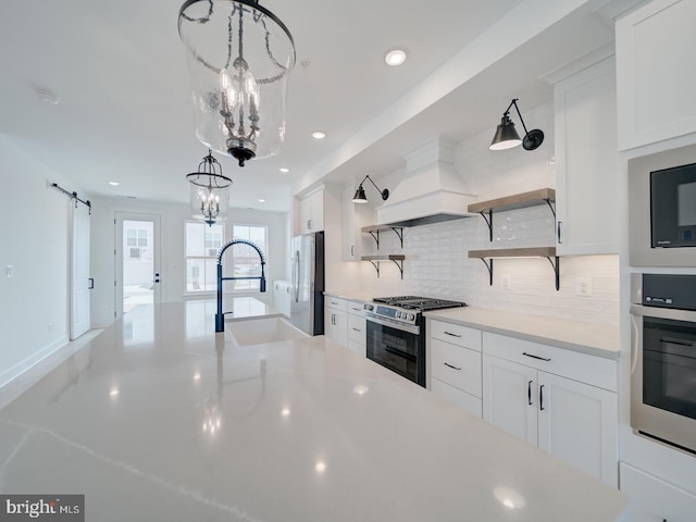 kitchen featuring a barn door, stainless steel appliances, premium range hood, open shelves, and a sink