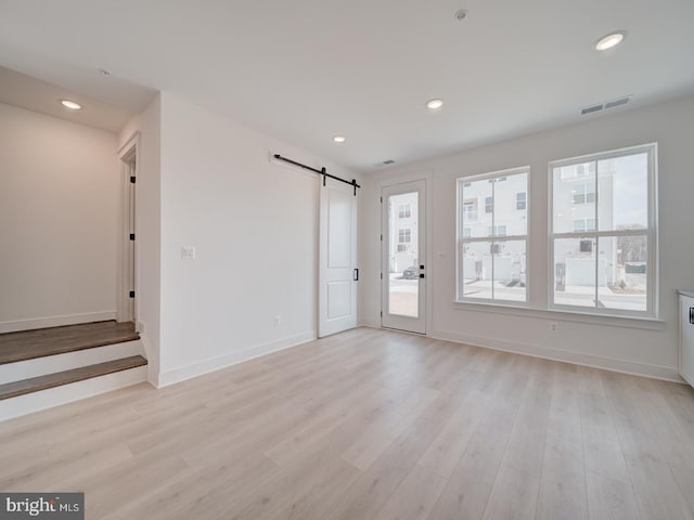 interior space featuring a barn door, visible vents, baseboards, light wood-type flooring, and recessed lighting