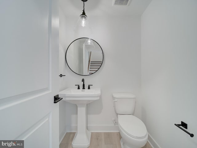 half bathroom with toilet, baseboards, visible vents, and wood finished floors