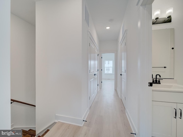 hall with recessed lighting, light wood-type flooring, a sink, and baseboards