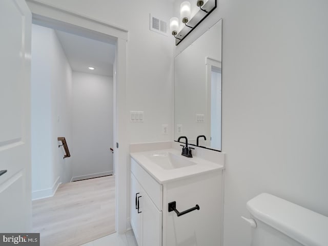 bathroom featuring visible vents, toilet, vanity, wood finished floors, and baseboards