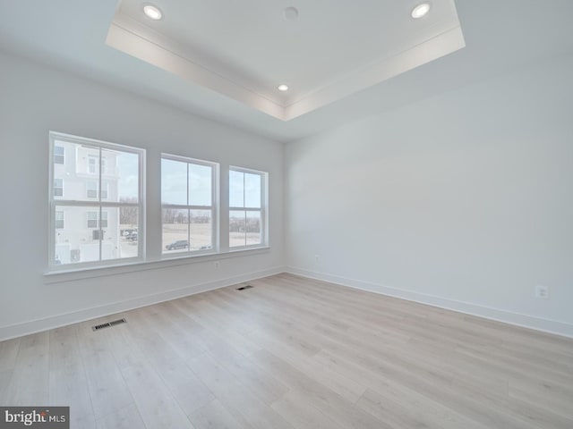 empty room with visible vents, a tray ceiling, light wood-style flooring, and baseboards