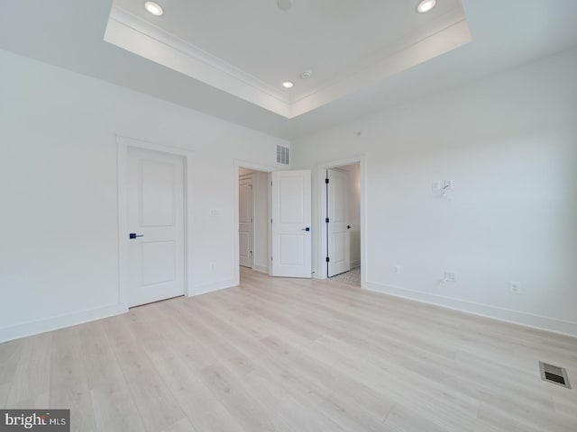 unfurnished bedroom with a tray ceiling, light wood-style flooring, visible vents, and baseboards