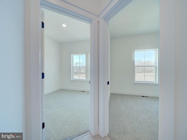 corridor with carpet floors, plenty of natural light, visible vents, and baseboards