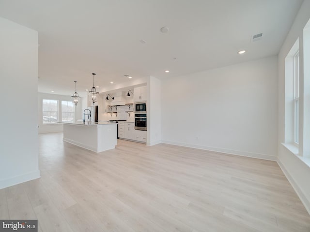 unfurnished living room with light wood finished floors, visible vents, baseboards, a sink, and recessed lighting