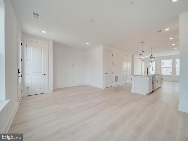 unfurnished living room with light wood-type flooring, visible vents, a sink, and recessed lighting