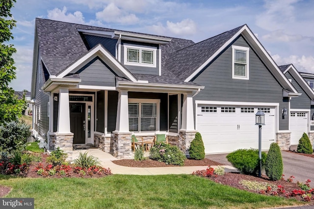 craftsman-style house featuring stone siding, covered porch, roof with shingles, and driveway