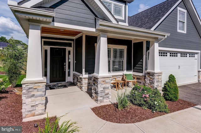 view of exterior entry featuring a porch, stone siding, a shingled roof, and a garage