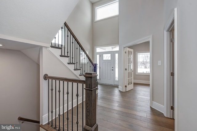 foyer entrance with a towering ceiling, baseboards, dark wood finished floors, and a wealth of natural light