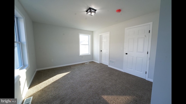 unfurnished bedroom featuring visible vents, dark carpet, and baseboards