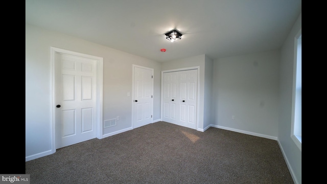 unfurnished bedroom featuring baseboards, visible vents, dark colored carpet, and a closet