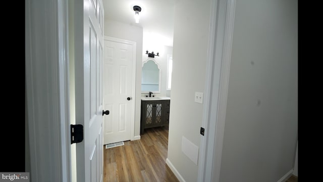 hallway with a sink, visible vents, and light wood-style floors