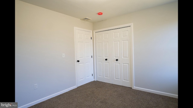 unfurnished bedroom featuring a closet, visible vents, dark carpet, and baseboards