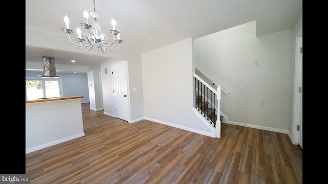 unfurnished living room with stairs, a chandelier, wood finished floors, and baseboards