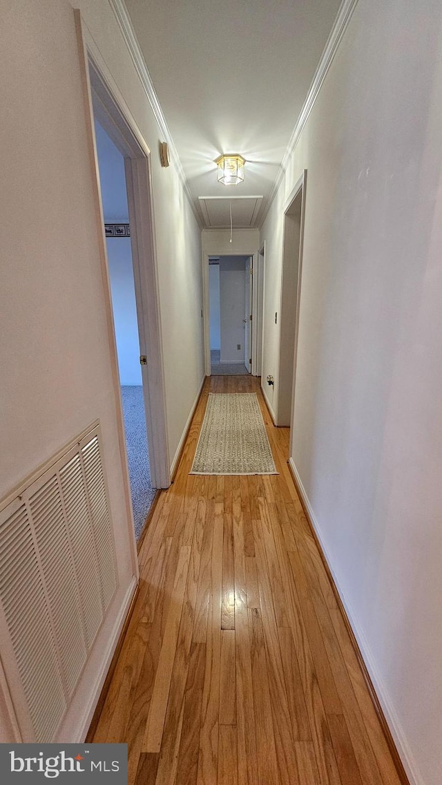 corridor with crown molding, visible vents, attic access, light wood-style floors, and baseboards