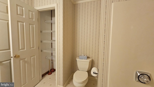 bathroom featuring toilet, wallpapered walls, and baseboards