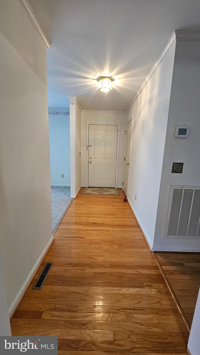 hall with light wood-style flooring, visible vents, and ornamental molding