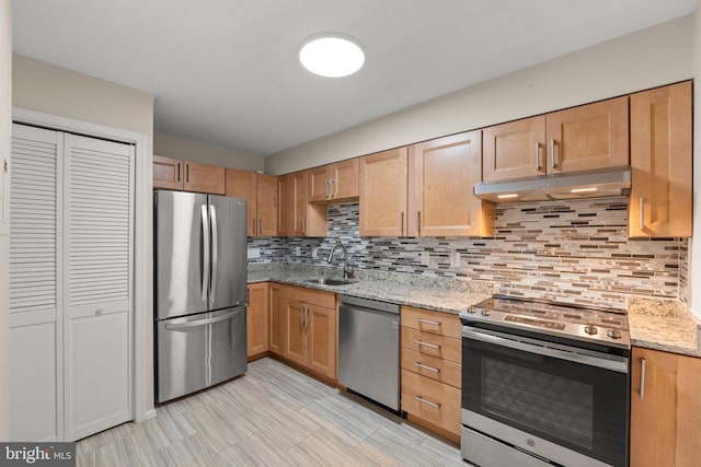 kitchen featuring tasteful backsplash, appliances with stainless steel finishes, light stone countertops, under cabinet range hood, and a sink