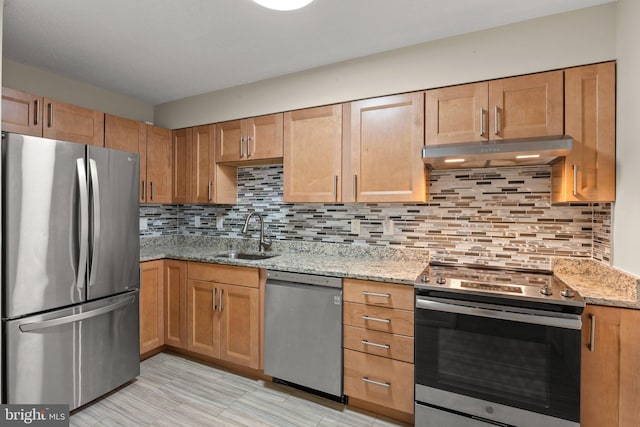 kitchen featuring decorative backsplash, light stone counters, stainless steel appliances, under cabinet range hood, and a sink