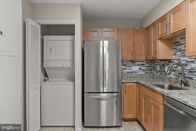 kitchen with tasteful backsplash, appliances with stainless steel finishes, stacked washer / dryer, a sink, and light stone countertops