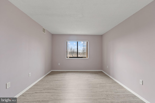 empty room with visible vents, light wood-style flooring, baseboards, and a textured ceiling