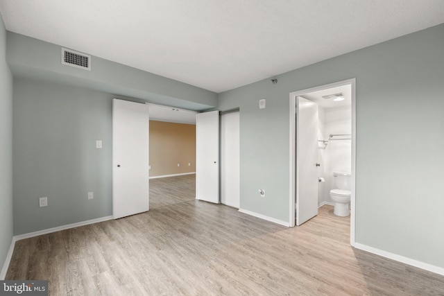 unfurnished bedroom with baseboards, connected bathroom, visible vents, and wood finished floors