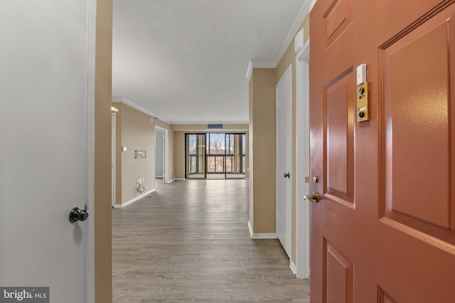 hallway featuring baseboards, a textured ceiling, light wood-style flooring, and crown molding