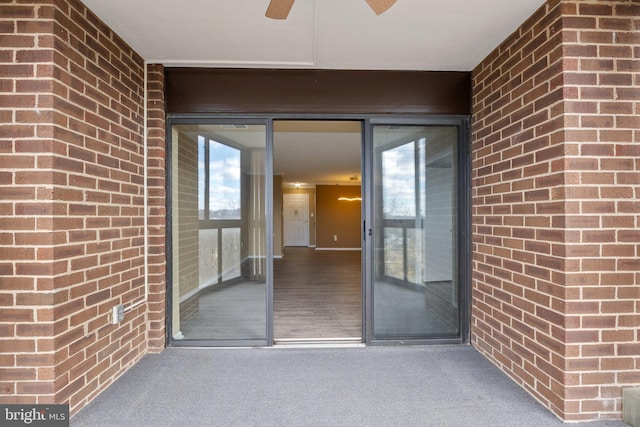 doorway to property featuring brick siding and a ceiling fan