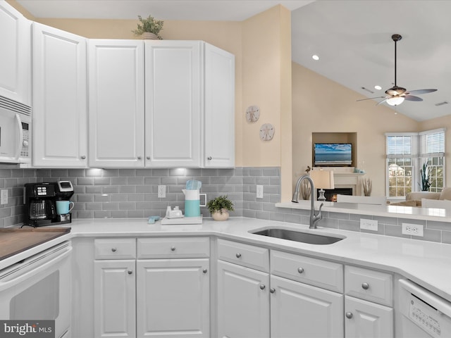 kitchen with white appliances, a sink, vaulted ceiling, white cabinets, and tasteful backsplash