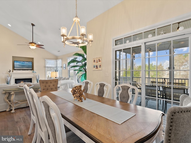 dining room with wood finished floors, high vaulted ceiling, a glass covered fireplace, and ceiling fan with notable chandelier